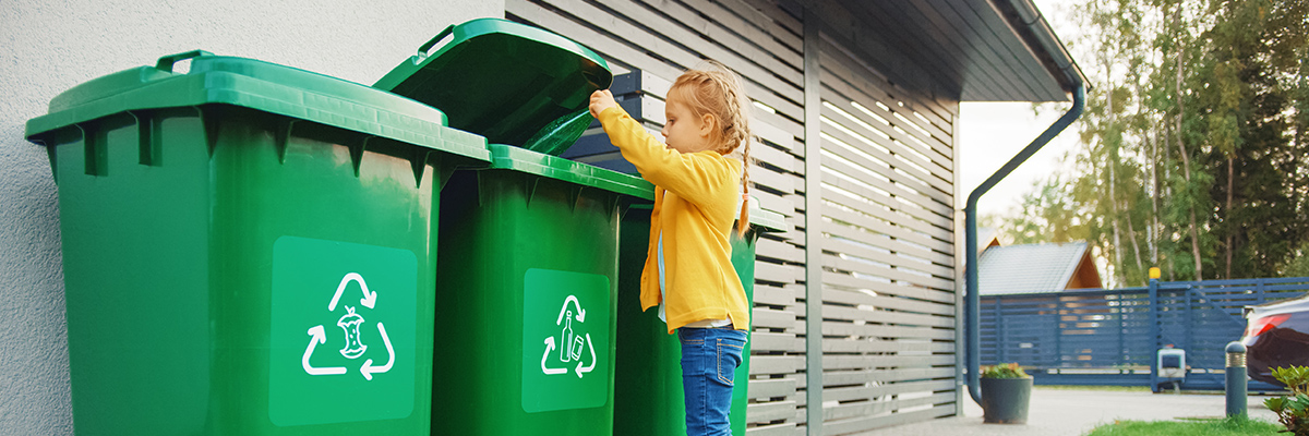 Child placing an item in recycle bin on side of house