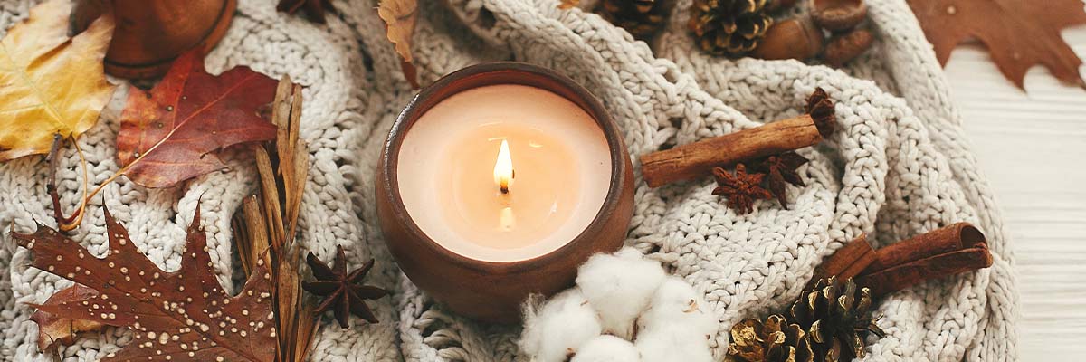 Seasonal candle burning next to scarf and leaves