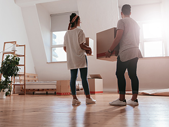 Couple holding moving boxes in house